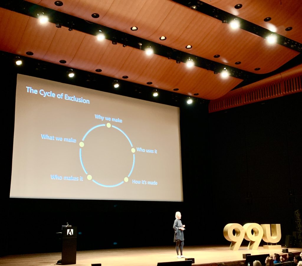 A person stands on stage presenting a talk titled The Cycle of Exclusion. The slide features a circular diagram connected to experience design, highlighting: What we make, Who makes it, Why we make it, Who uses it, and How its made.