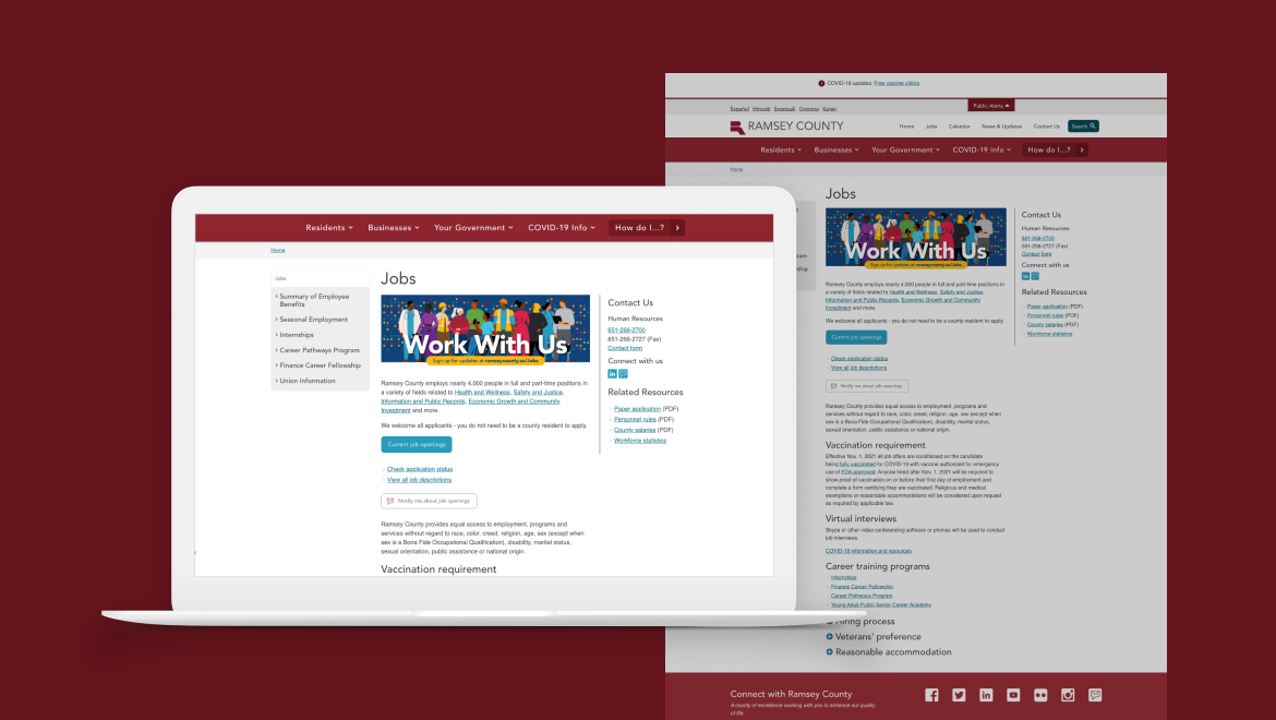 A laptop showcasing the Ramsey County jobs webpage with a Work With Us banner highlights the seamless user experience. The screen features navigation menus and job-related links, while a desktop monitor in the background echoes this digital solution, all set against a striking red backdrop.