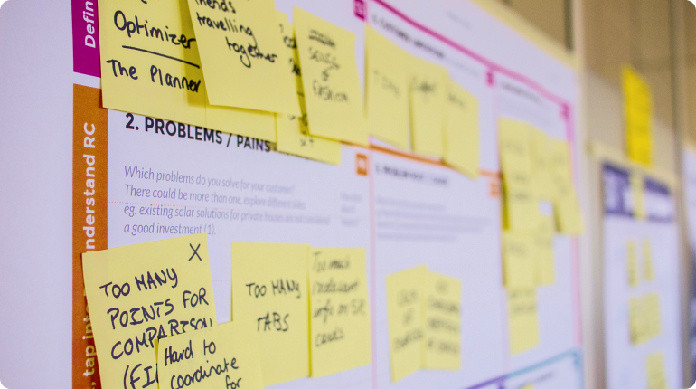 Close-up of a board covered with sticky notes featuring various handwritten notes and ideas, focusing on organizing and solving problems to enhance user experience. The background shows printed text with headings for Problems/Pains and Understand RC, emphasizing a Clockwork approach to solutions.