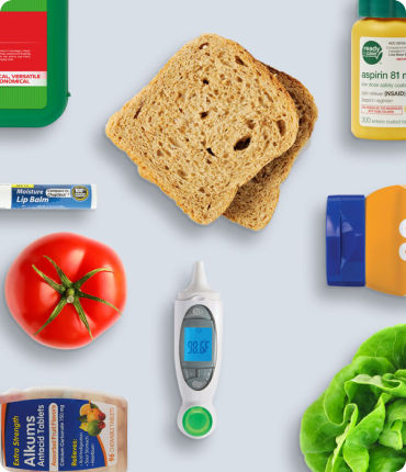 A flat lay on a light blue background showcases an assortment of items: whole wheat bread, a tomato, lettuce, chicken broth carton, aspirin, lip balm, and a thermometer showing 98.6°F. This curated arrangement delivers a seamless user experience in everyday essentials.