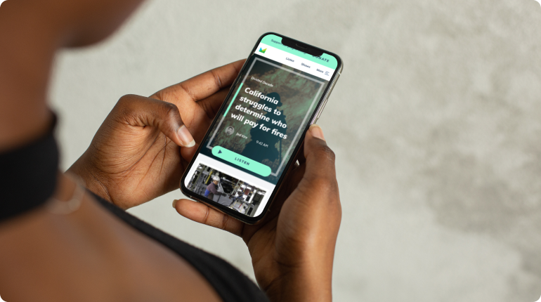 A person is holding a smartphone displaying a news article titled California Struggles to Determine Who Will Pay for Fires. The article, enriched by experience design, includes an image of a forest. The persons finger hovers, ready to scroll through the engaging digital solution.
