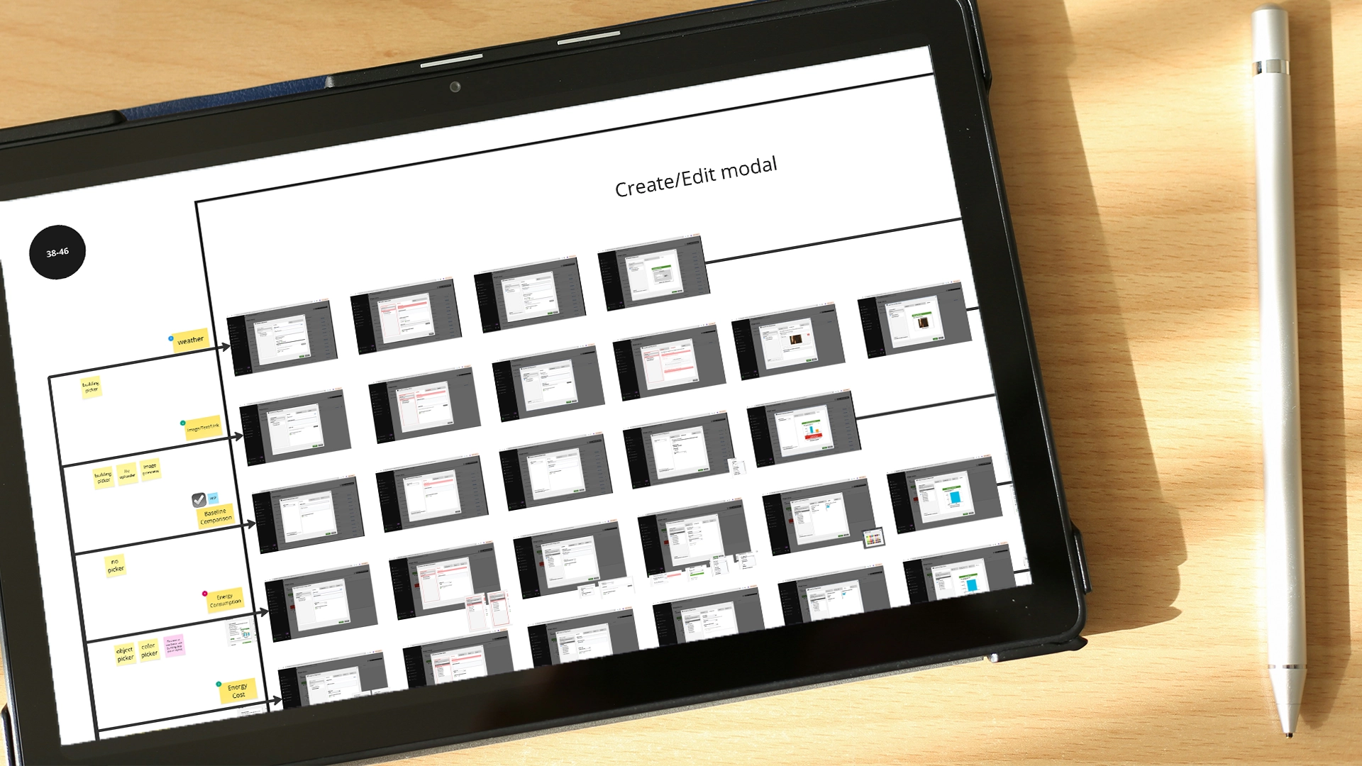A tablet displays a flowchart titled Create/Edit modal with multiple small screenshot thumbnails. The device rests on a wooden surface beside a silver pen in bright natural light.