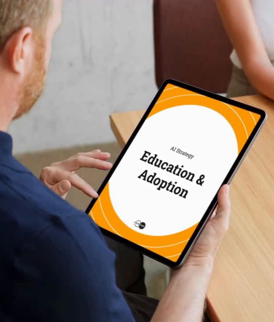 A person holding a tablet displaying a document titled AI Strategy: Education & Adoption with an orange and white design, seated at a table with another person nearby.